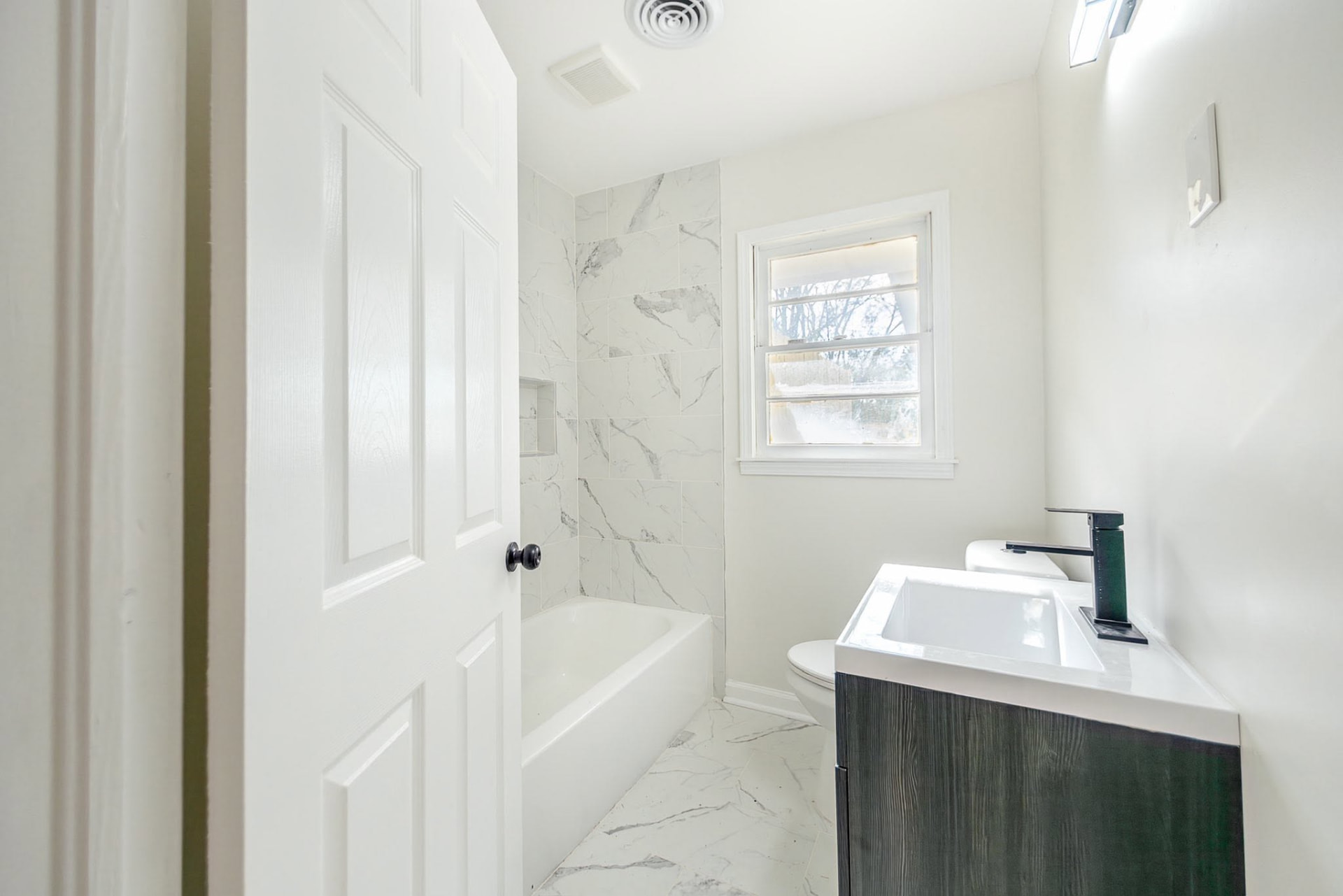 Remodeled bathroom with marble-look tile and dark wood vanity in a Stellar-managed home